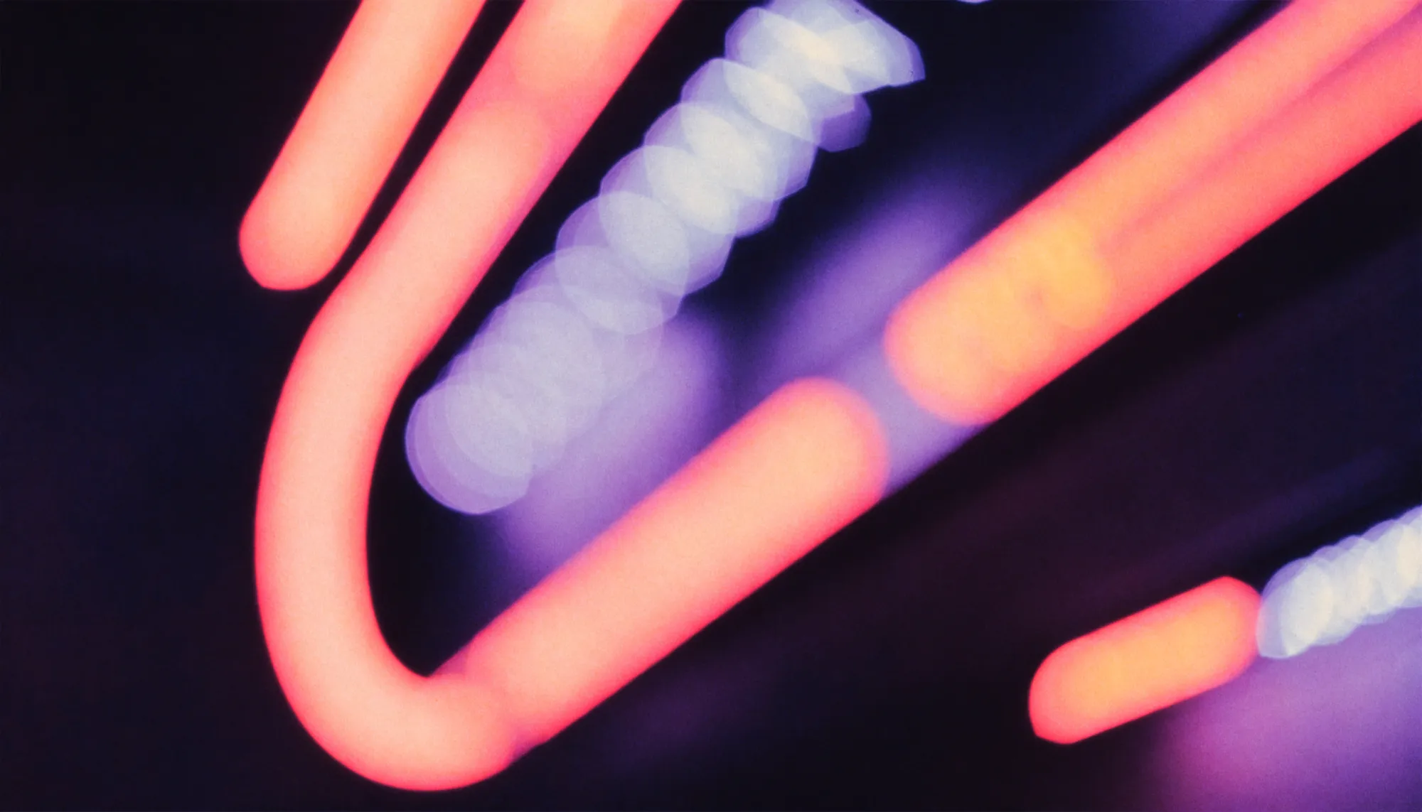 Blurred pink and coral neon tubes glowing against the dark